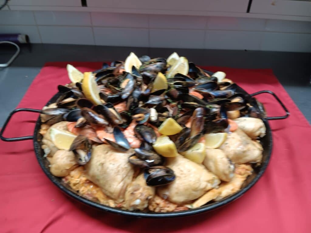 Paella royale garnie de moules, morceaux de poulet, crevettes et quartiers de citron dans un plat traditionnel.