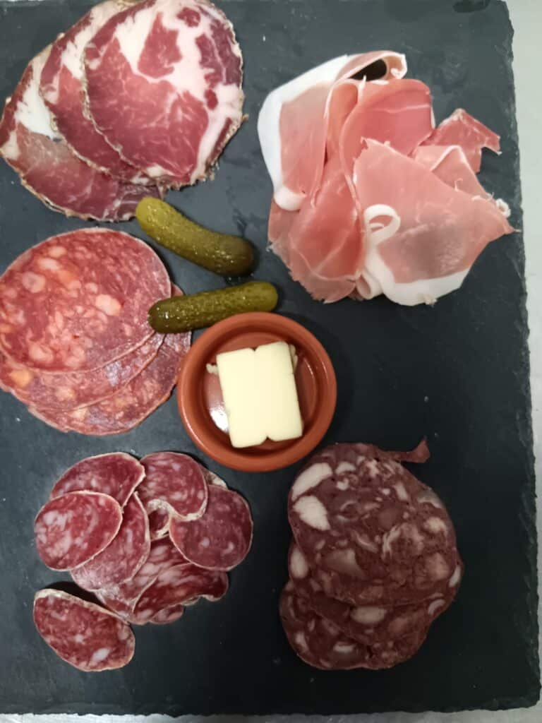 Planche de Charcuterie Garnie avec Jambon et Saucisson Assortiment de charcuterie fine avec jambon cru, saucisson, chorizo et cornichons sur une planche d'ardoise noire.