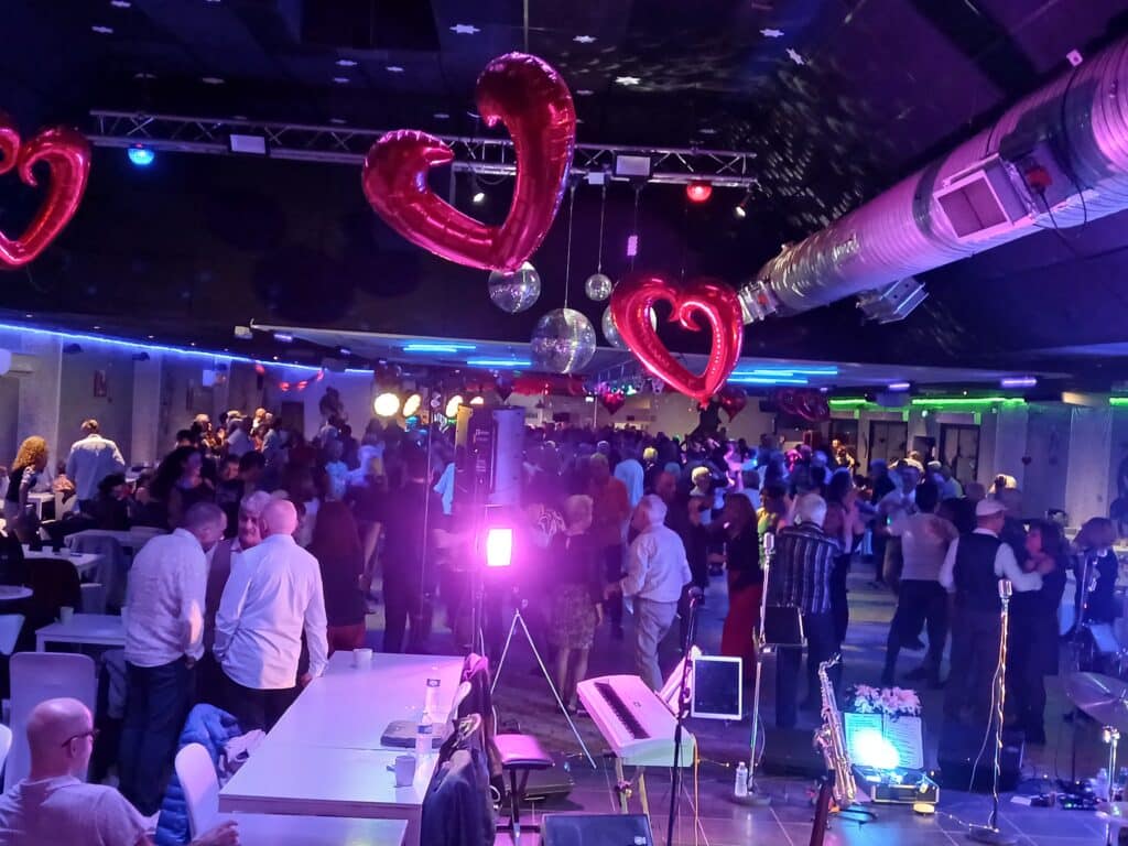 Soirée dansante festive avec ballons cœurs rouges, boules à facettes et éclairage néon violet dans une salle animée.