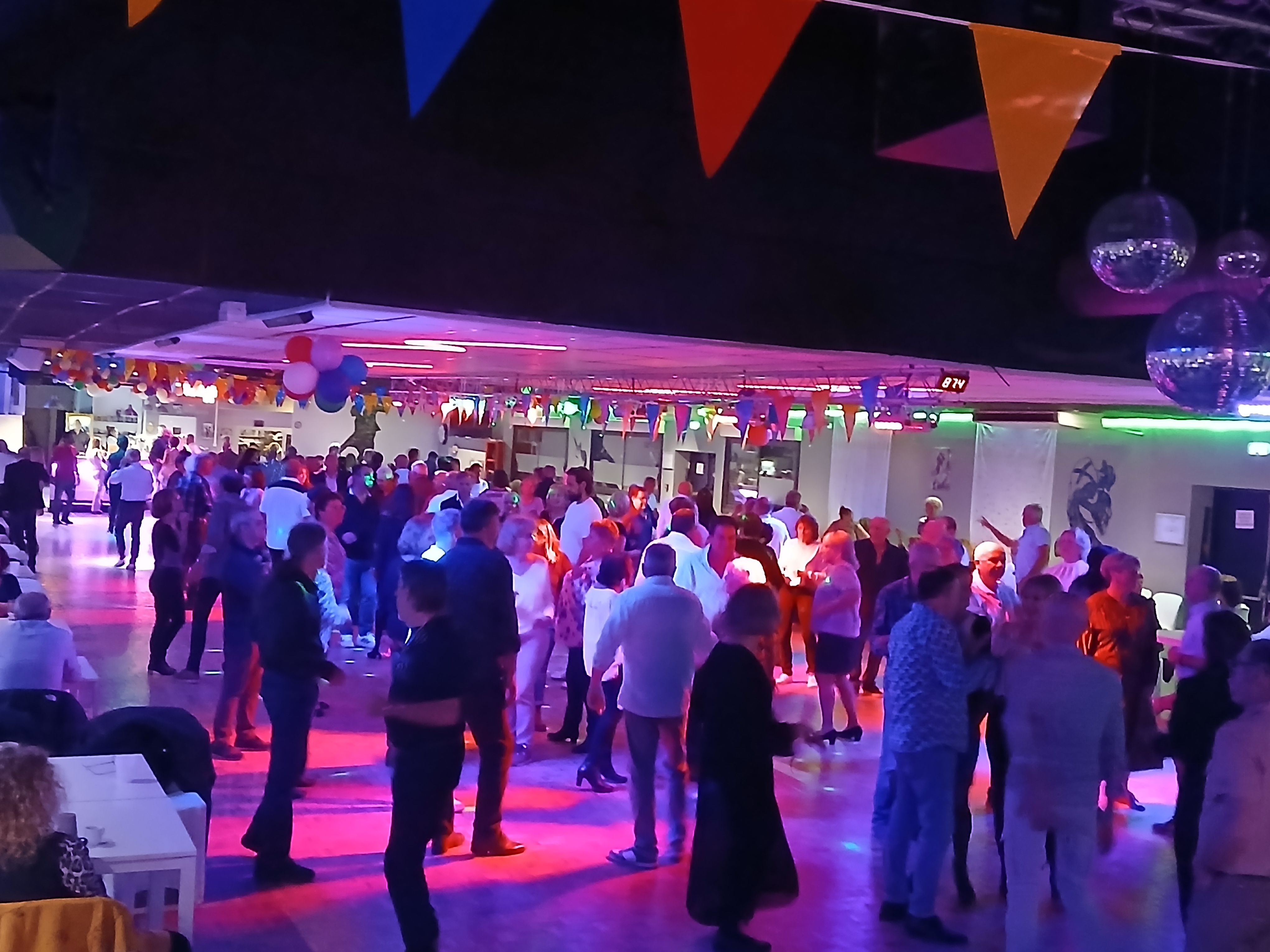 Soirée Dansante Festive sous des Lumières Colorées Gens dansant sur une piste colorée sous des fanions et boules à facettes lors d'une fête festive.
